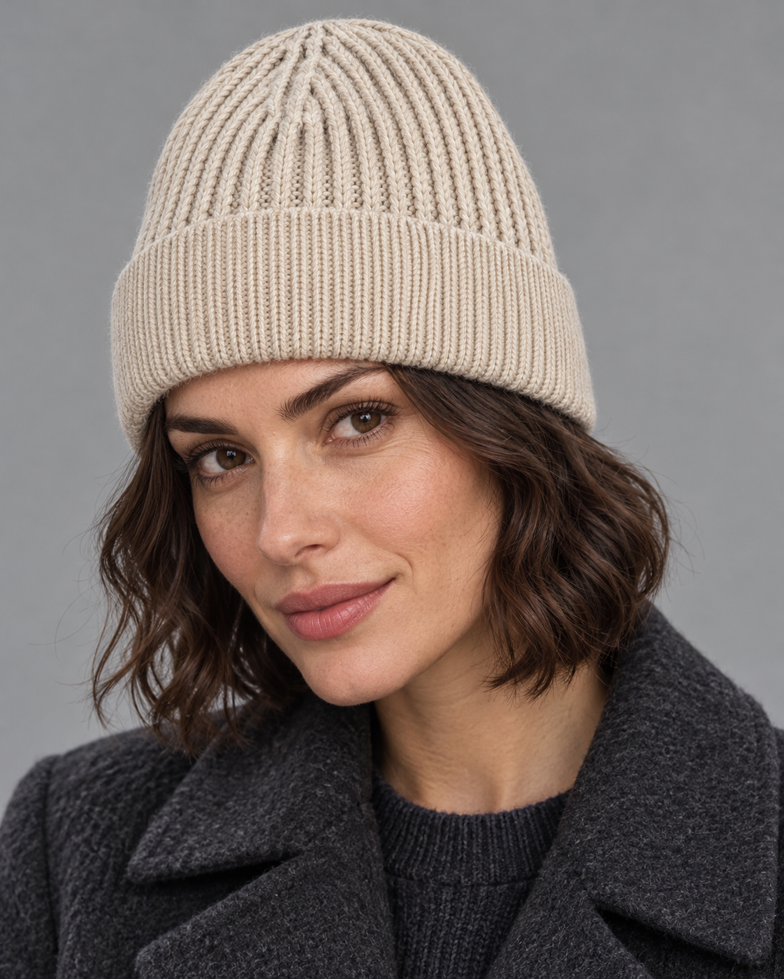 Woman wearing the light beige s.Oliver textured knit beanie with a charcoal coat in a studio portrait.