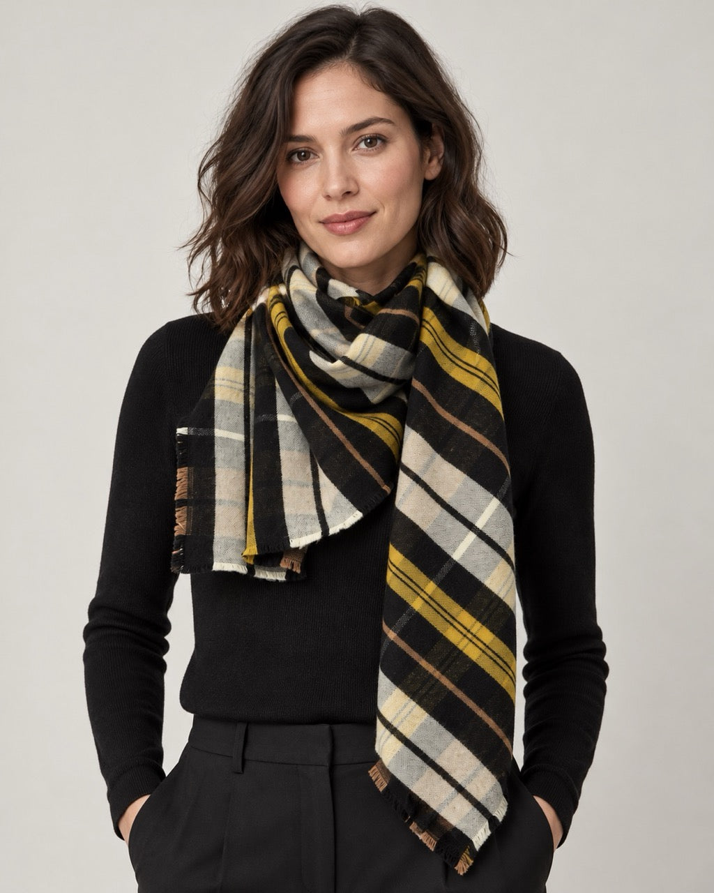 Model wearing an s.Oliver square scarf with black, mustard yellow, cream and grey checks over a black top against a neutral background.