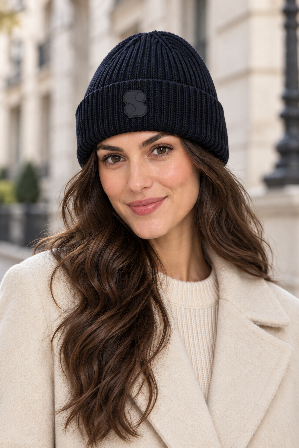 Woman styling the s.Oliver navy blue ribbed beanie with a light coat on a city street